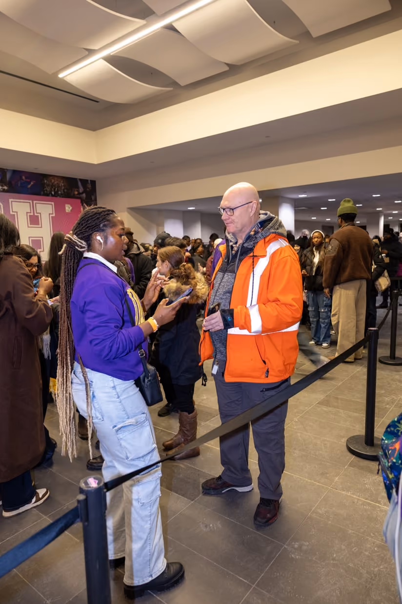 A volunteer in a high-visibility jacket talking with a guest in the venue foyer.